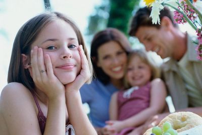 A girl smiling with her family enjoying a picnic outdoors.