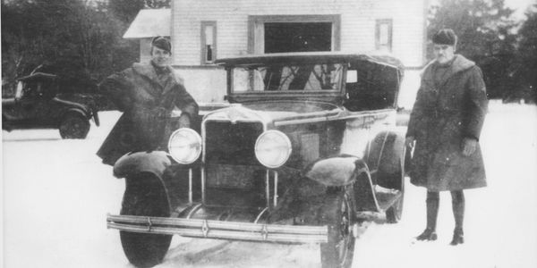 Two men stand beside a vintage car in the snow.
