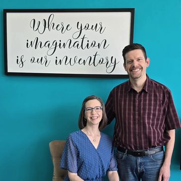Couple smiling in front of a teal wall with an inspirational sign.