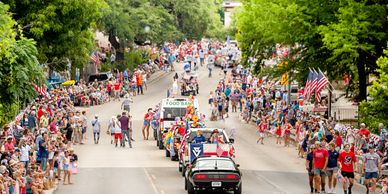A lively parade with crowds lining the streets on a sunny day.