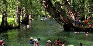 People swimming and relaxing in a shaded, tree-lined natural waterway.