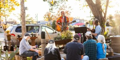 Outdoor live music with a small audience seated on benches and stools.
