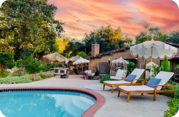 Cozy backyard with pool, lounge chairs, and umbrellas at sunset.