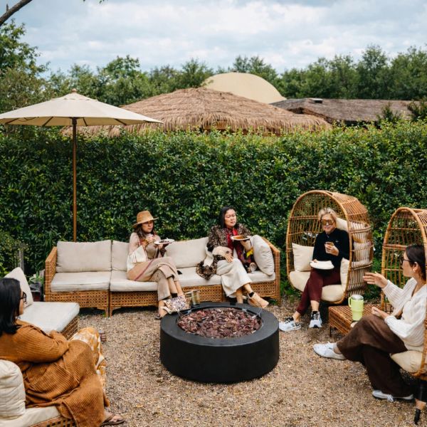 Group of friends enjoying food and drinks outdoors around a fire pit.