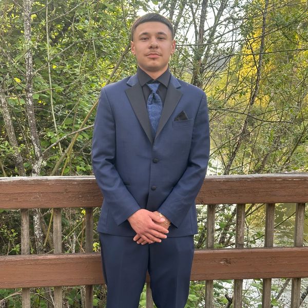 Young man in a blue suit standing outdoors on a wooden bridge.