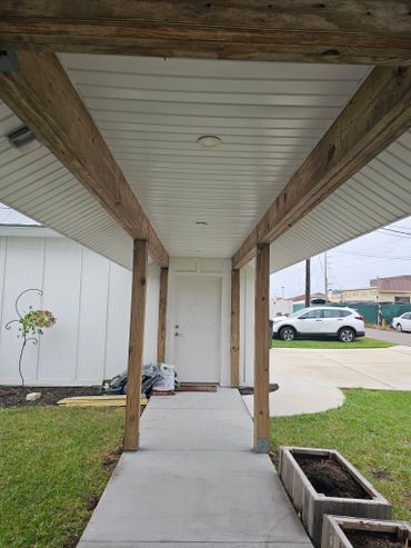 Covered porch leading to a white door with wooden beams and planters.