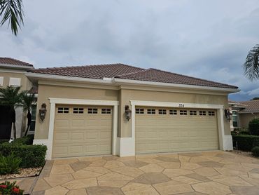 Two beige garage doors on a suburban house under a cloudy sky.