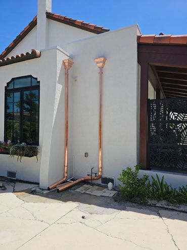 Copper downspouts installed on a white stucco house exterior.