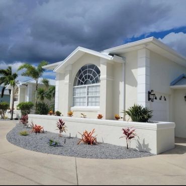 Modern house with large arched window and landscaped garden under cloudy sky.