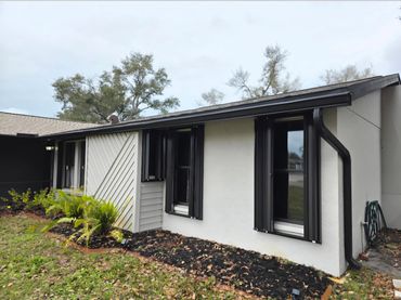 Modern single-story house with black window shutters and light-colored exterior.