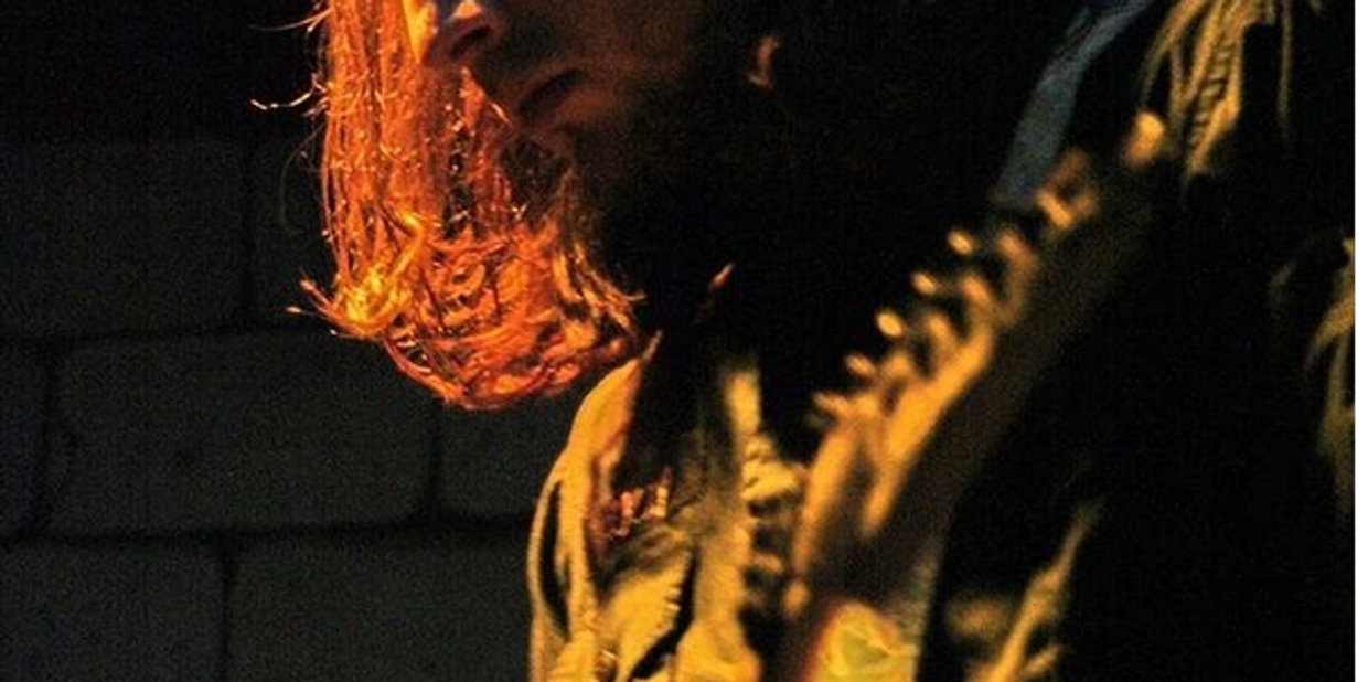 Man with long hair playing electric guitar under warm light.