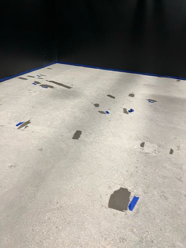 Concrete floor with multiple patches marked by blue tape in a dark room.