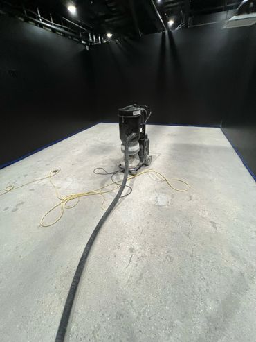 A vacuum cleaner on a concrete floor in a dimly lit black-walled room.