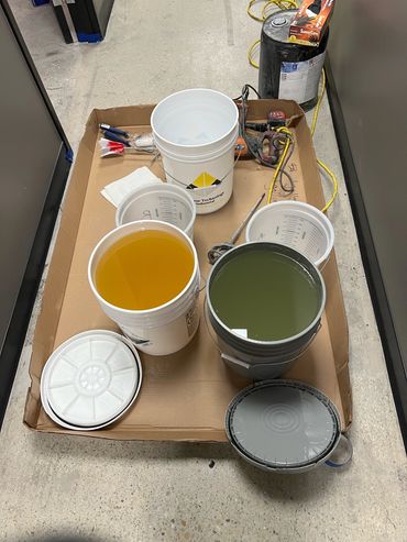 Buckets filled with colored liquids and tools on a cardboard surface.