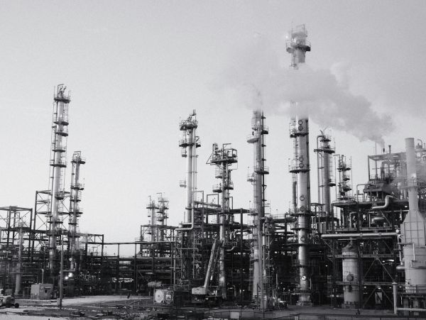 Black and white image of an industrial refinery emitting smoke.