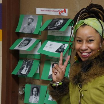 Dr. Lindo giving a peace sign beside a picture of herself in a school's Black History project.