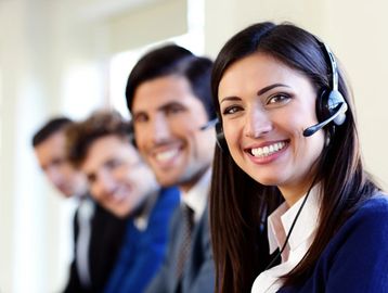 A smiling woman in a headset with colleagues in the background.