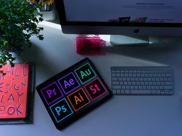 Workspace with Apple computer, keyboard, and tablet showing Adobe software icons.