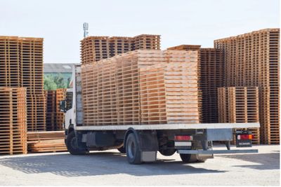 Truck loaded with wooden pallets in an outdoor storage area.