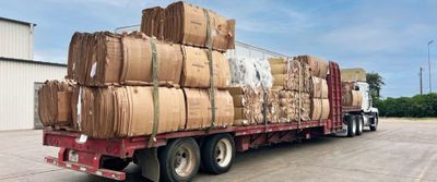 A flatbed truck loaded with large stacks of compressed cardboard and paper materials for recycling.