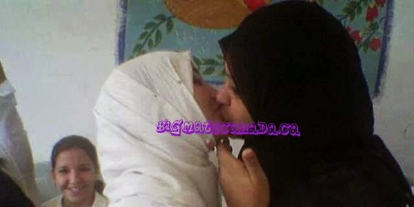 Two women wearing hijabs share a kiss, while another smiles in the background.