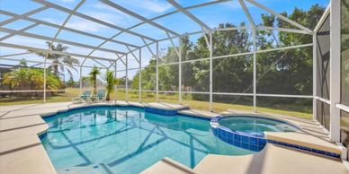 A screened-in outdoor pool with hot tub and tropical plants.