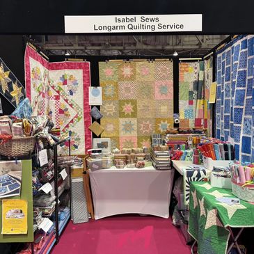Quilting service booth showcasing colorful handmade quilts and fabrics.