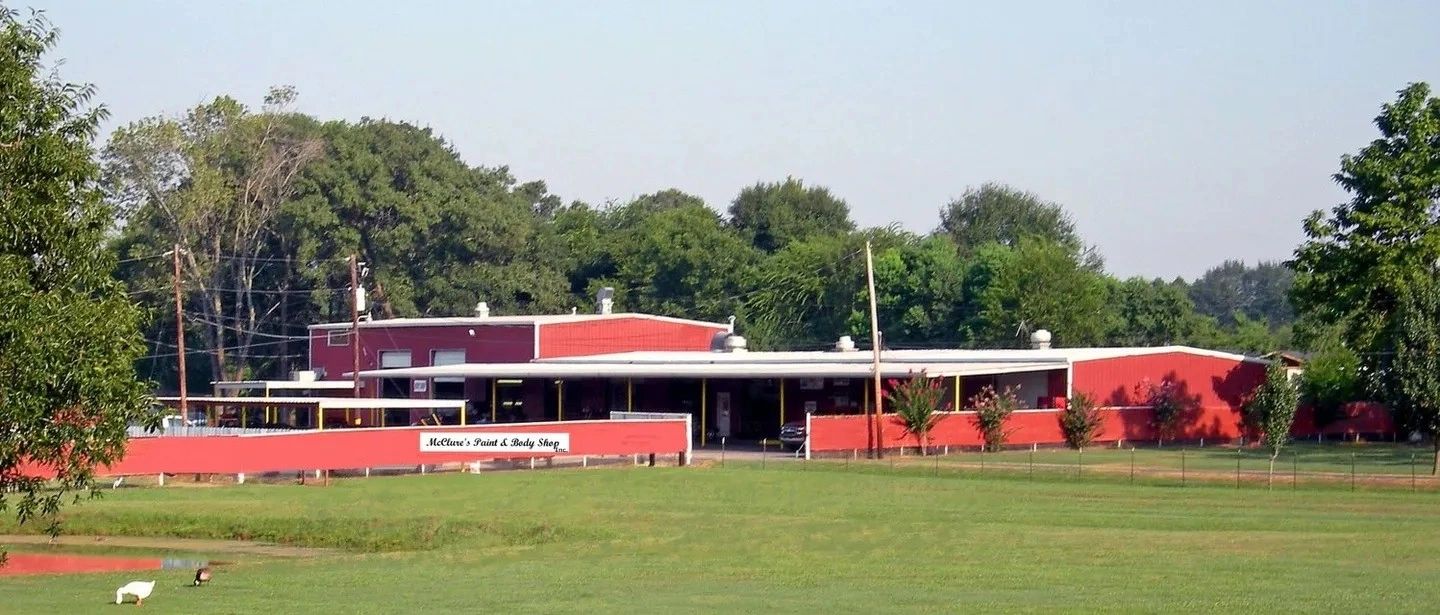 Red building with a green field and trees in the background.