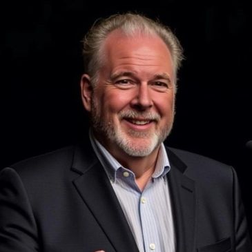 Smiling man in suit speaking at a podium against a dark background.