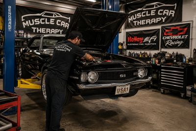Mechanic working on a classic Chevrolet muscle car in a garage.