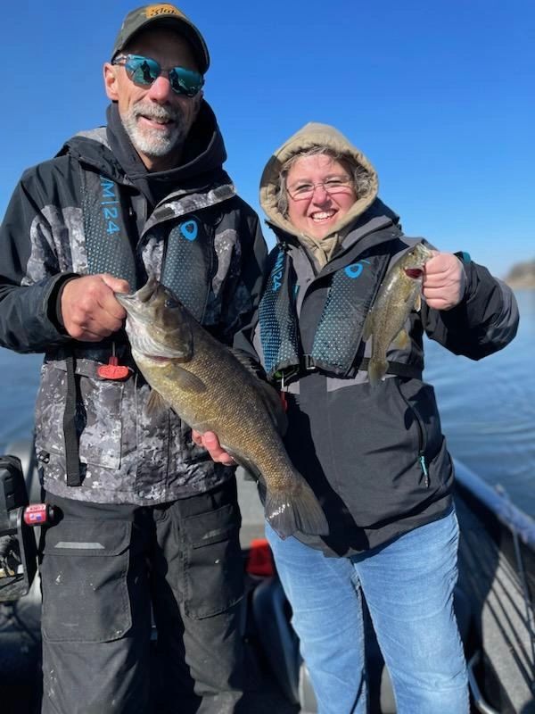 Two people proudly holding their catches on a fishing trip.