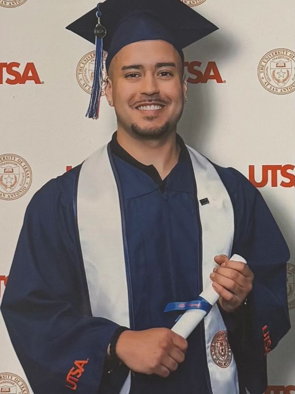 Graduate in cap and gown holding diploma, smiling at UTSA ceremony.