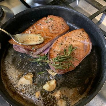 Duck breast frying in a pan being basted with rosemary garlic butter