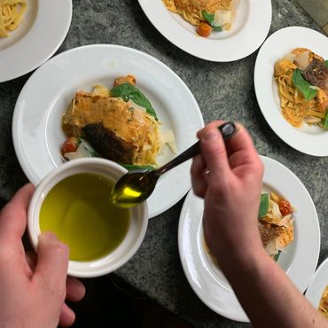 Olive oil being added to Tuscan salmon linguine for private dining guests