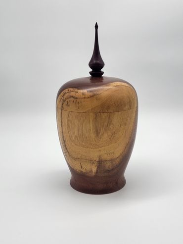 A polished wooden urn with a pointed finial on top.