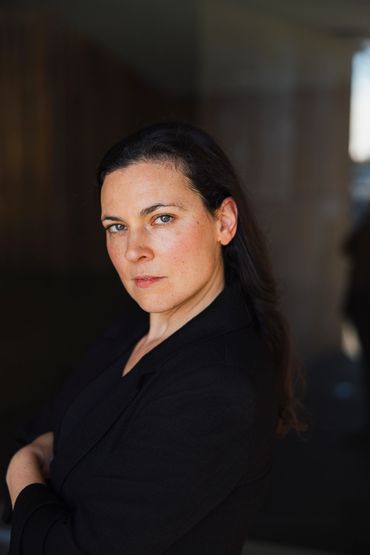 Confident woman with dark hair and a black blazer looks intently at the camera.