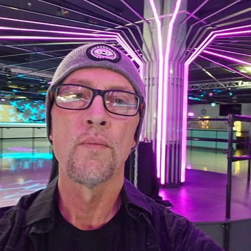 Man wearing glasses and a beanie with neon lights in the background.