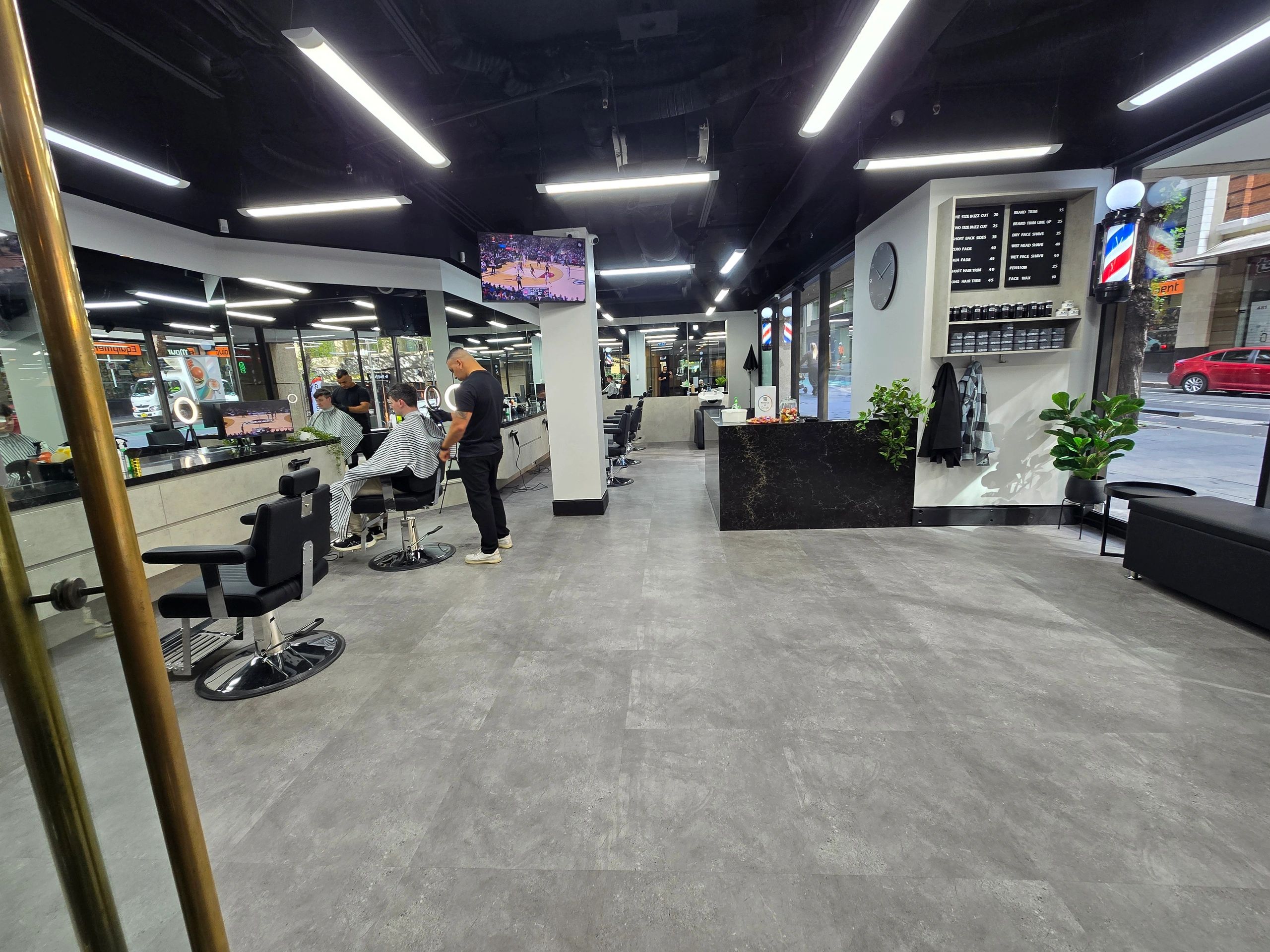 Modern barbershop with customers getting haircuts and NBA game on TV.