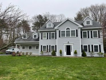 Large gray house with black shutters and green lawn.