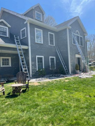 Gray house exterior being prepped for painting with ladders and drop cloths.