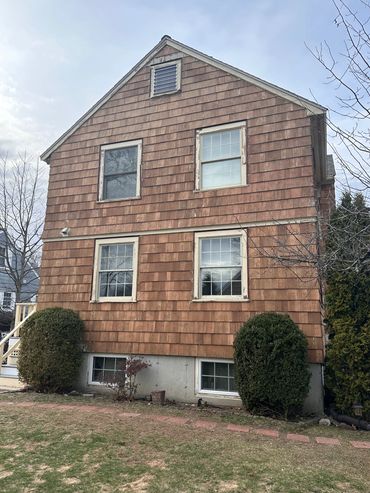 Weathered brown wooden house with multiple windows and bushes in front.