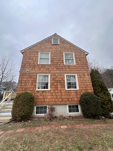Red wooden house exterior with windows and bushes under a cloudy sky.