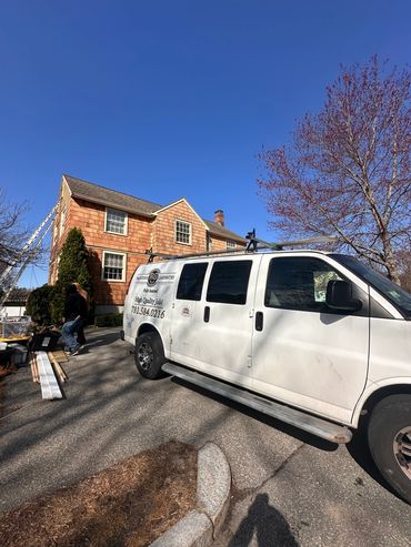 Van parked outside a house with workers and painting supplies under a clear blue sky.