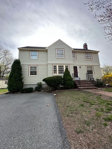 Two-story beige house with white-trimmed windows and a brick entrance staircase.