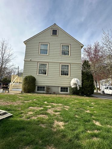 Side view of a beige house with four windows and a green lawn.