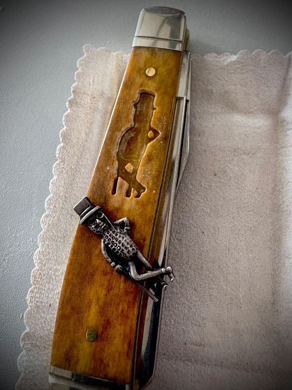Vintage folding knife with a wooden handle and a reclining metal figure decoration.