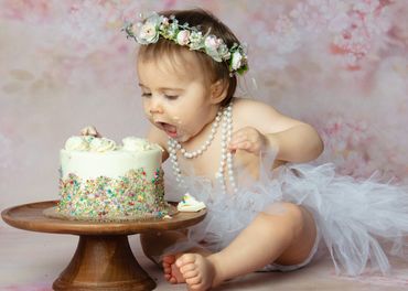 Baby attempting to eat cake for her first birthday cake smash photo shoot session. 