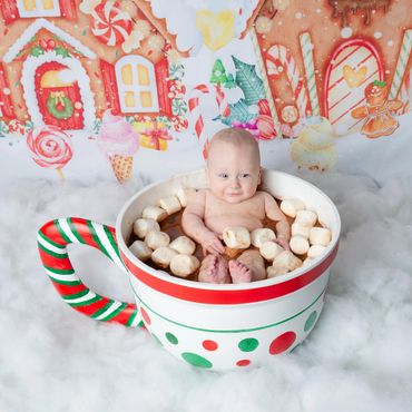 Baby smiling in a festive hot chocolate cup surrounded by marshmallows.