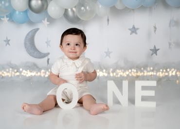 First birthday photoshoot with boy sitting on cake smash set decorated with moon and stars
