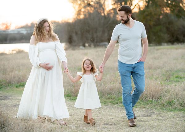 Parents hold hands with daughter during their outdoor maternity photography session in Austin, Texas.